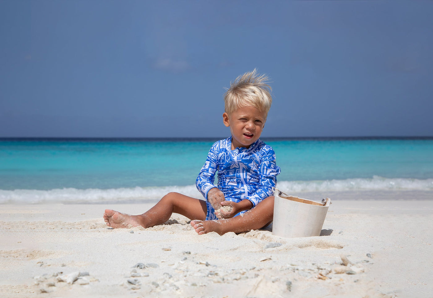 little brother and big brother on the beach wearing flap happy swim wear and hat holding surfbaord at the beach