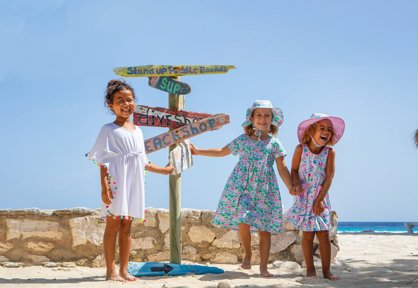 two girls at the beach wearing flap happy dresses. one with mermaids on them and the other pink sparkles. Theyre at the beach